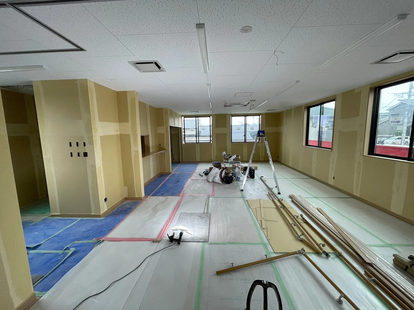 2階の部屋の内装仕上げ中。窓の並ぶ壁とボードの下地、床の養生